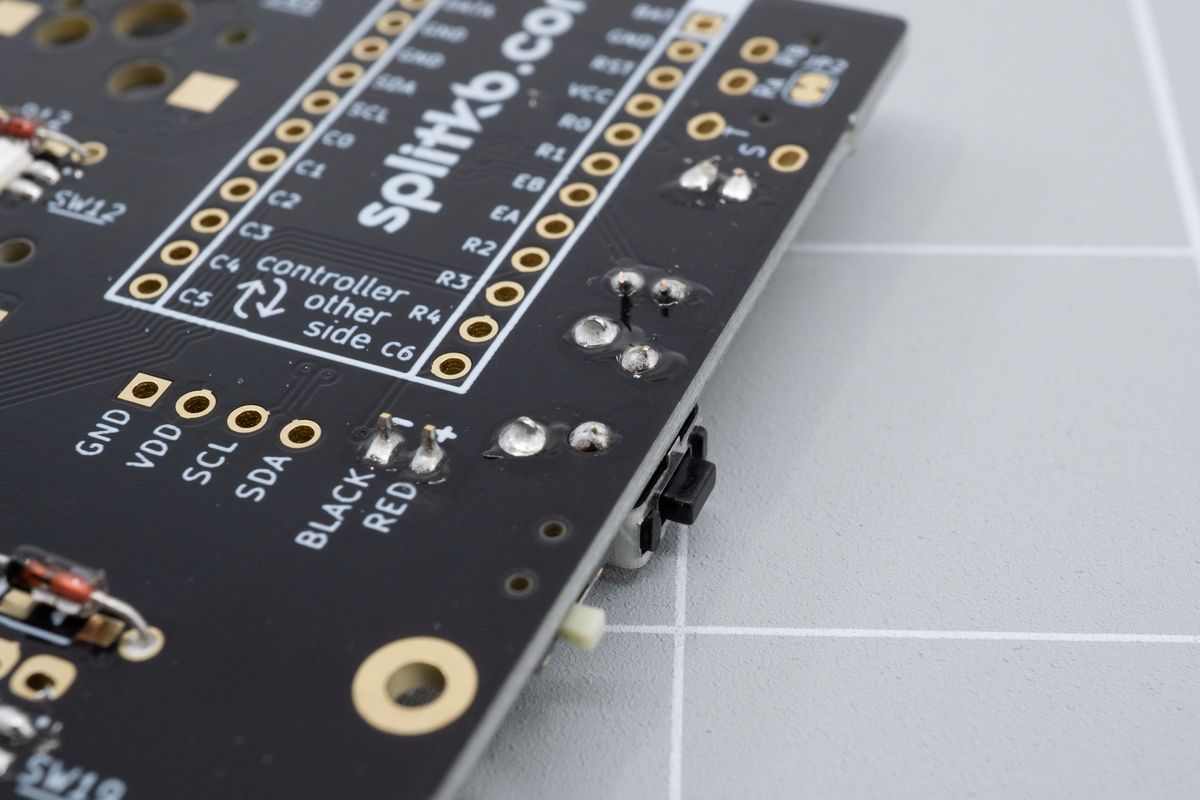 The angled reset button, soldered, looking from the bottom side of the PCB